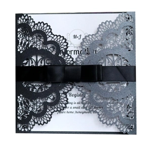Close-up of laser cut wedding invitation with black and silver glitter lace and ribbon