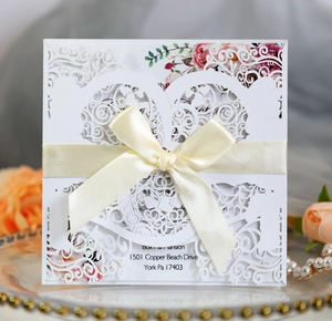Detail of laser-cut wedding invitation with silk bow and floral print on pearlescent paper