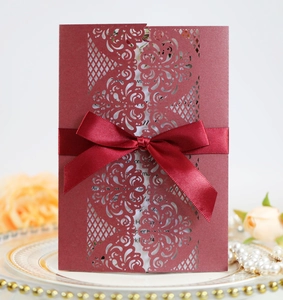 Detailed laser-cut burgundy wedding invitation with elegant satin bow on luxury plate