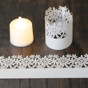 Laser cut snowflake paper sleeve for LED tea lights on dark wood background