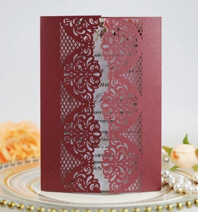 Close-up of burgundy laser-cut floral wedding invitation on elegant ceramic tray