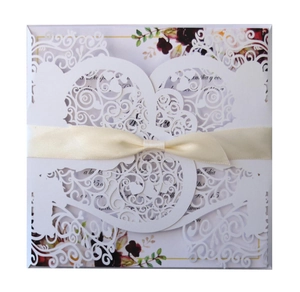 Detail view of laser-cut wedding invitation with silk ribbon bow and floral pattern