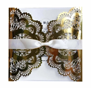 Detailed laser-cut floral pattern on gold glitter wedding invitation with white ribbon