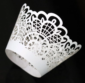 Macro shot of laser-cut white lace cupcake wrapper with intricate geometric hollow design