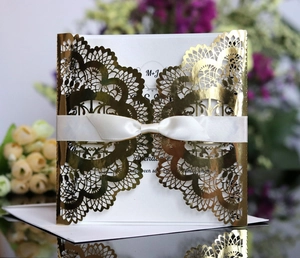 Macro view of gold laser-cut floral wedding invitation with white silk bow and inner card