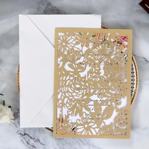 Détail du motif floral découpé au laser sur faire-part de mariage doré avec enveloppe