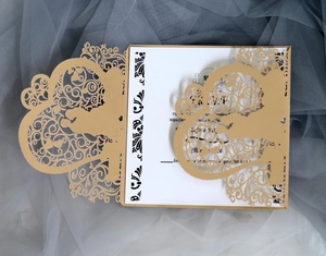 Detail of laser-cut gold wedding invitation with elegant heart patterns and inner card