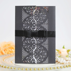 Detail of laser-cut floral pattern on black paper invitation sleeve with silk ribbon bow