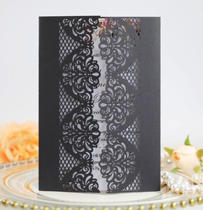 Detail of laser-cut black wedding invitation sleeve with floral patterns on a porcelain plate