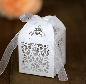 Close-up of white laser-cut wedding favor box with heart patterns and satin ribbon bow