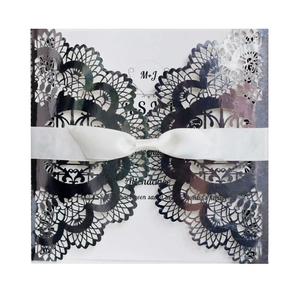 Detail of laser-cut navy wedding invitation featuring intricate floral patterns and a white bow