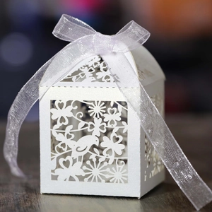 Detail of white laser-cut wedding candy box with bird patterns and purple ribbon