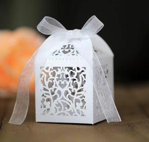Detail of white laser-cut wedding favor box with heart patterns and sheer ribbon bow