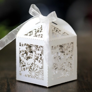 Close-up of laser-cut wedding candy box with bird and floral patterns and white ribbon