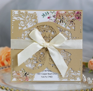 Detail of laser-cut gold wedding invitation with a cream ribbon and floral inner card