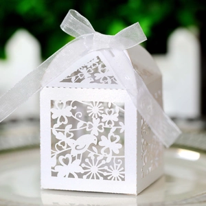 Detail of laser-cut wedding favor box with bird patterns and white organza ribbon bow