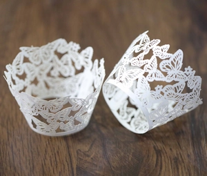 Detail of white laser-cut cupcake wrappers with intricate butterfly patterns on wood