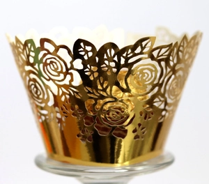 Golden laser-cut cupcake wrappers with rose patterns on a glass display stand