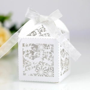 Intricate laser-cut bird and floral patterns on white paper wedding favor box with ribbon