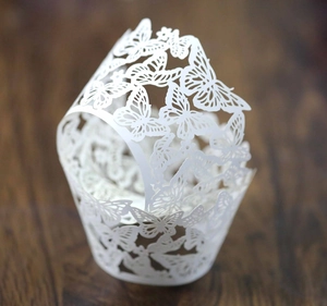 Detail of laser-cut white butterfly lace paper wrapper for wedding cupcakes on wood