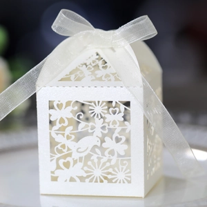 Detail of white laser-cut favor box featuring bird patterns and a white silk ribbon