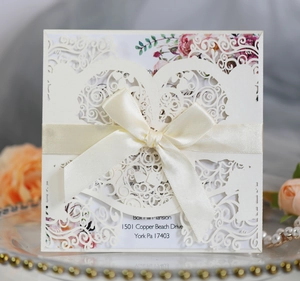 Detail of ivory laser-cut wedding invitation with heart patterns and satin bow decoration