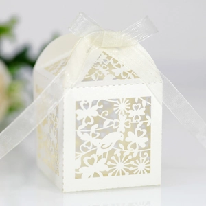 Detail of white laser-cut favor box with bird patterns and decorative silk ribbon