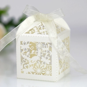 Detail of laser-cut white favor box featuring intricate bird and floral patterns and ribbon