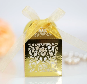 Detailed laser-cut gold wedding favor box with intricate heart patterns and ribbon bow