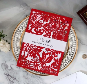 Invitation de mariage rouge découpée au laser avec motif floral sur une surface de marbre