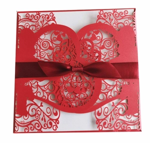 Detail of red laser-cut wedding invitation cover with intricate floral patterns and ribbon
