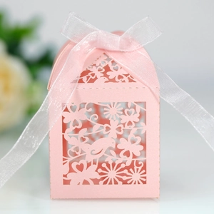 Detail of pink laser-cut wedding favor box with bird and floral patterns and ribbon