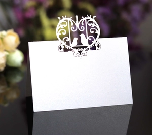 Macro detail of white pearlescent wedding table card with laser-cut heart and bird pattern