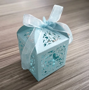 Top view of a light blue laser-cut gift box with a glossy ribbon bow on a wooden table