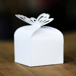 Detailed macro view of a white laser-cut butterfly wedding favor box on a wooden table
