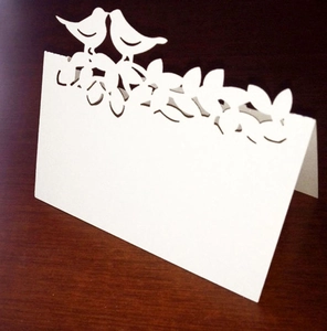 Détail d'un marque-place de mariage découpé au laser avec oiseaux et motifs floraux blancs