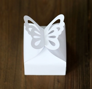 Top view of a white wedding favor box with a laser-cut 3D butterfly on a wood background