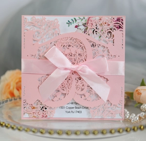 Detailed laser-cut pink wedding invitation with a satin bow on a decorative glass tray