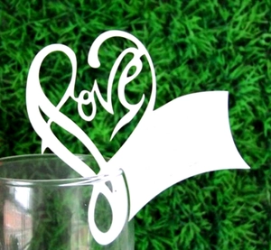 Close-up of laser-cut white heart card with LOVE design on a glass rim for parties