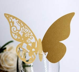 Detail of laser-cut gold butterfly place card on a wine glass with floral cutouts