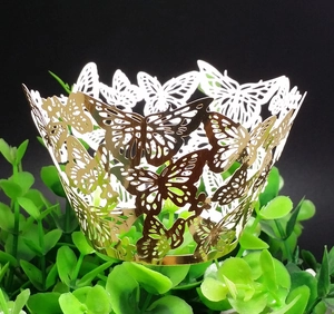 Macro detail of laser-cut gold butterfly cupcake wrappers on green leaves with black background