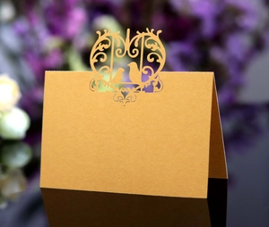 Detailed laser-cut heart and bird patterns on a golden pearlized wedding place card