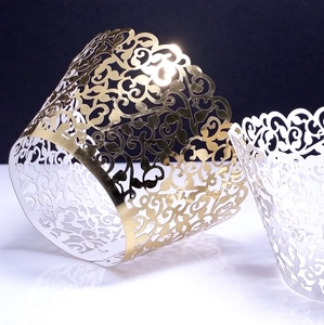 Close-up of laser-cut vine patterns on white and gold pearlized cupcake wrappers