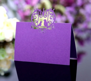 Close-up of laser-cut purple place card featuring intricate birds and heart scroll design