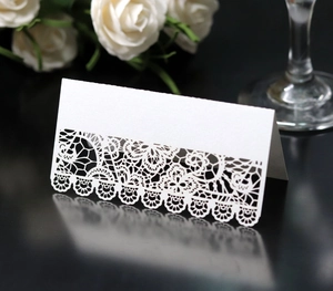 Detail of white laser-cut lace place card with floral patterns on an elegant table