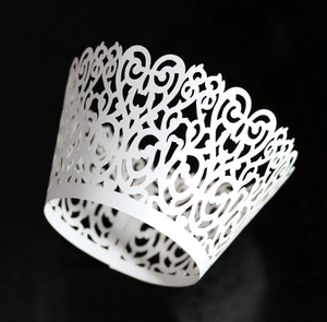 Detailed laser-cut white cupcake wrapper with elegant floral vine pattern on black background