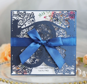 Laser-cut navy blue wedding invitation with satin bow and floral inner card