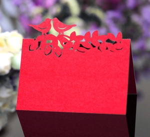 Détail d'un marque-place rouge découpé au laser avec motifs oiseaux et fleurs délicats