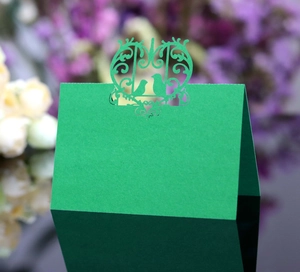 Detail of laser-cut green wedding place card with intricate birds and heart pattern