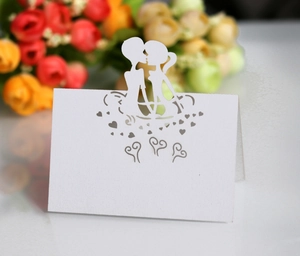 Detail of white laser-cut wedding place card featuring couple silhouette and heart patterns